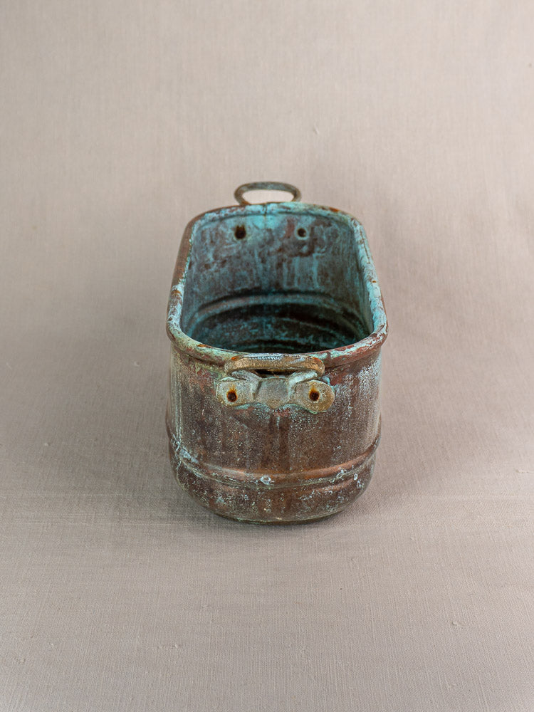 Antique French copper poissonnière jardinière with verdigris patina, dual front openings, back handle on beige background.