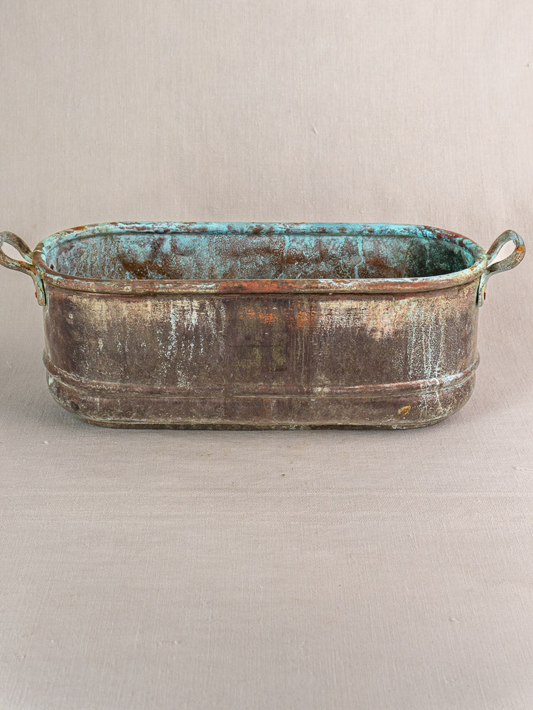 Antique French copper jardinière with verdigris patina, blue-green interior, and side handles on neutral fabric.