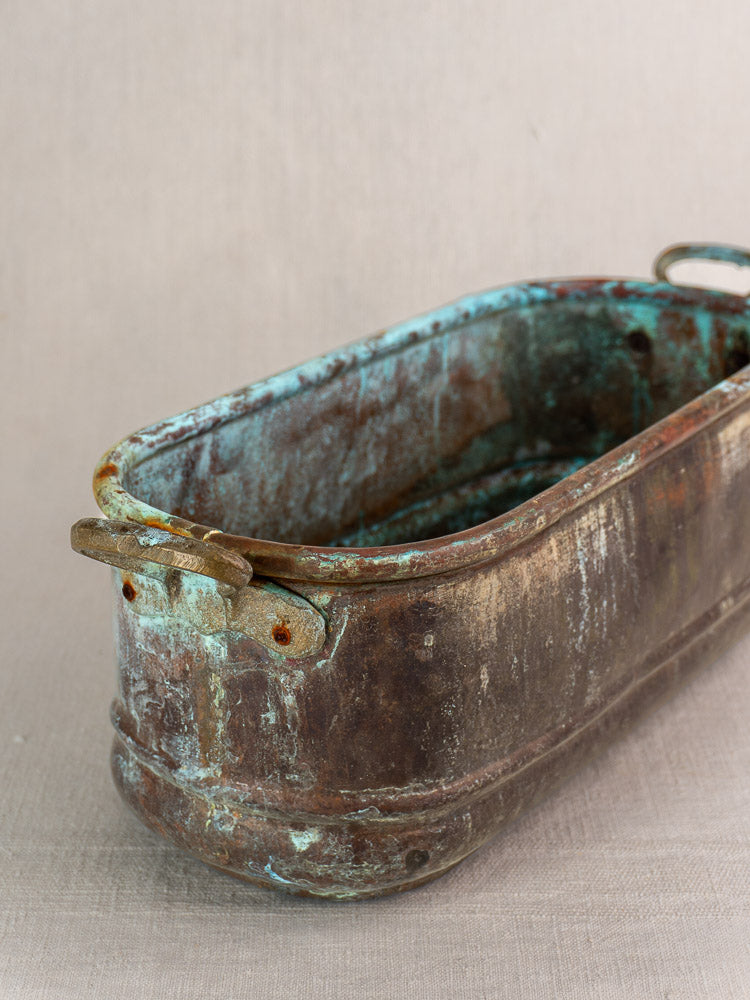 Antique French copper jardinière with verdigris patina and brass handles on neutral fabric background.