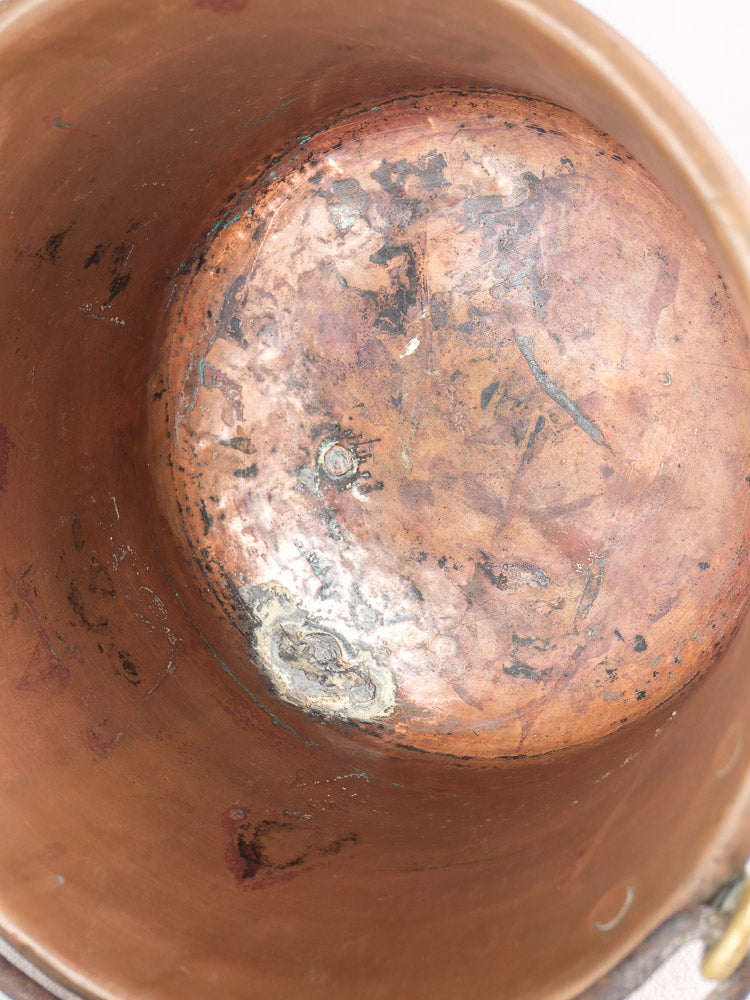 Interior of antique French copper hearth pot with iron bail handle, showing tarnish, stains, and corrosion.