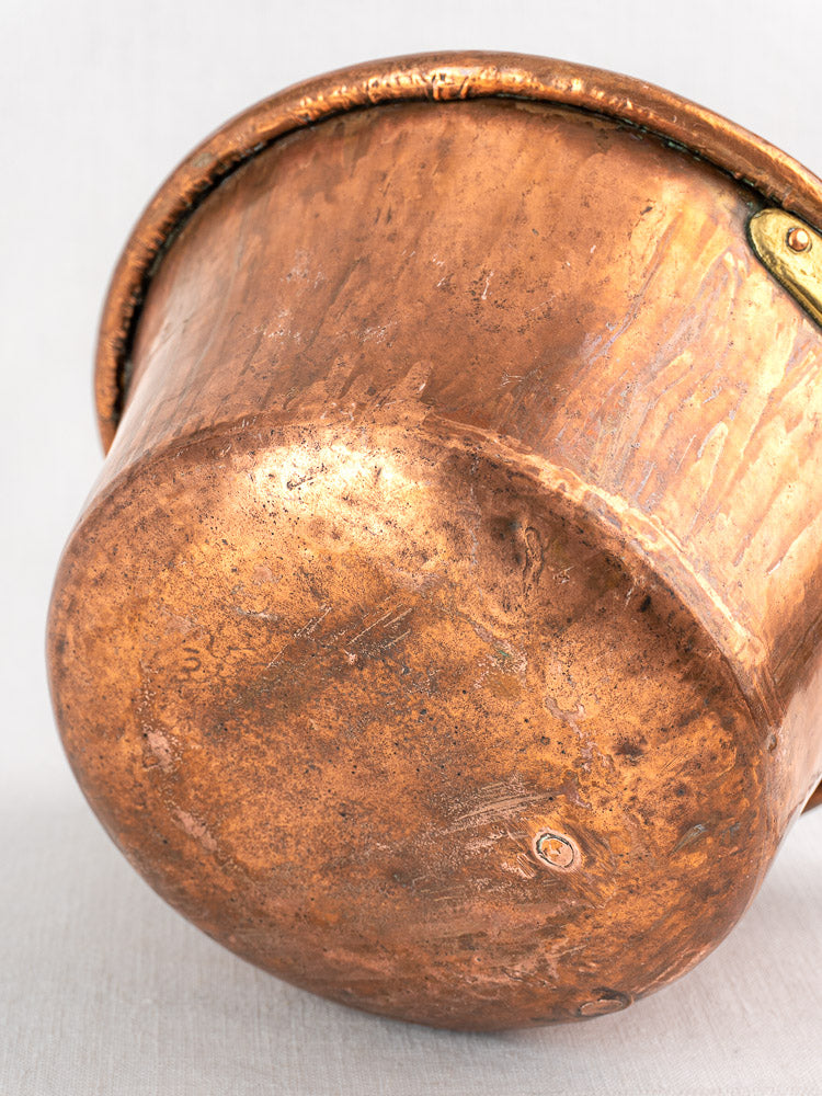 Antique French copper hearth pot showing patina and iron bail handle, tipped on light background.