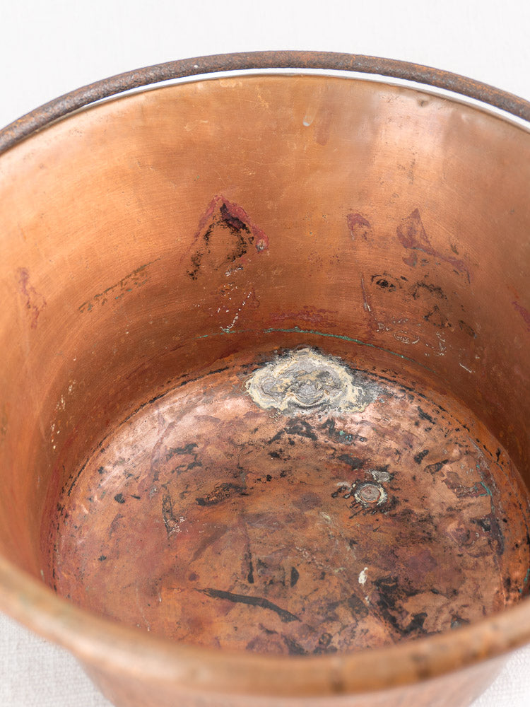 Close-up of antique French copper hearth pot interior with iron bail handle, chain, and aged patina.