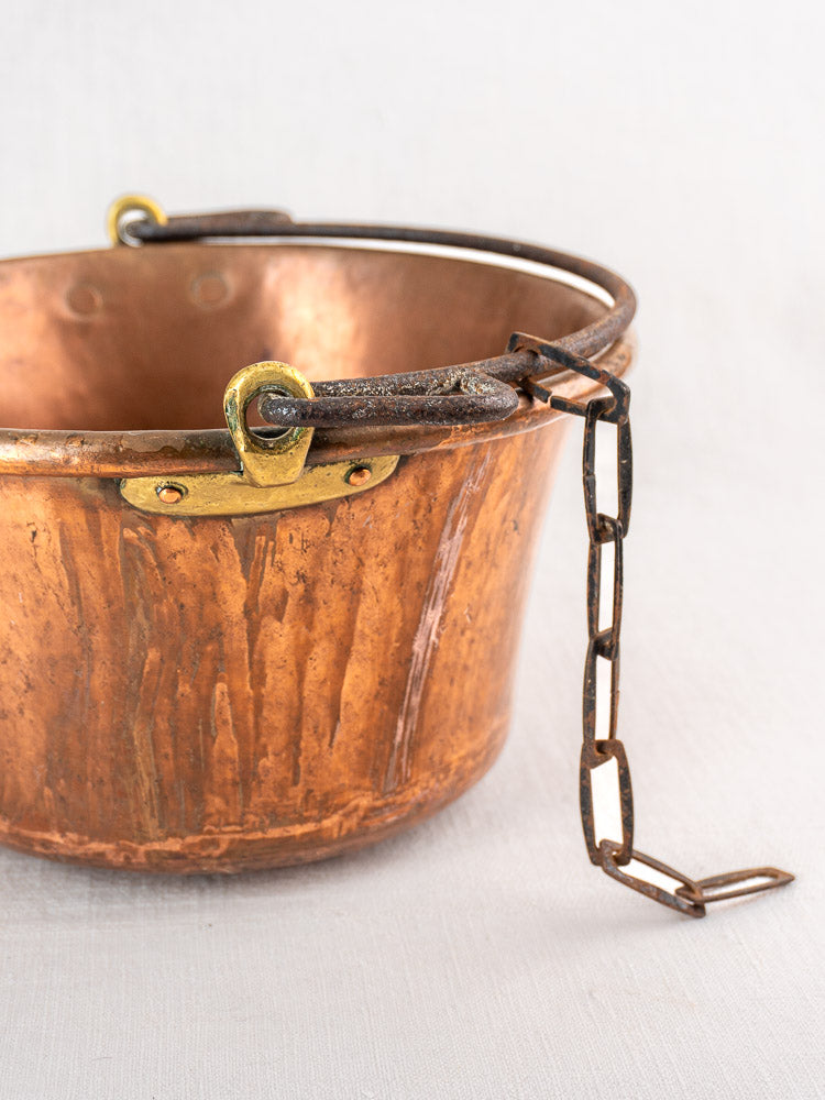 Antique French copper hearth pot with iron bail handle and chain on a light surface.