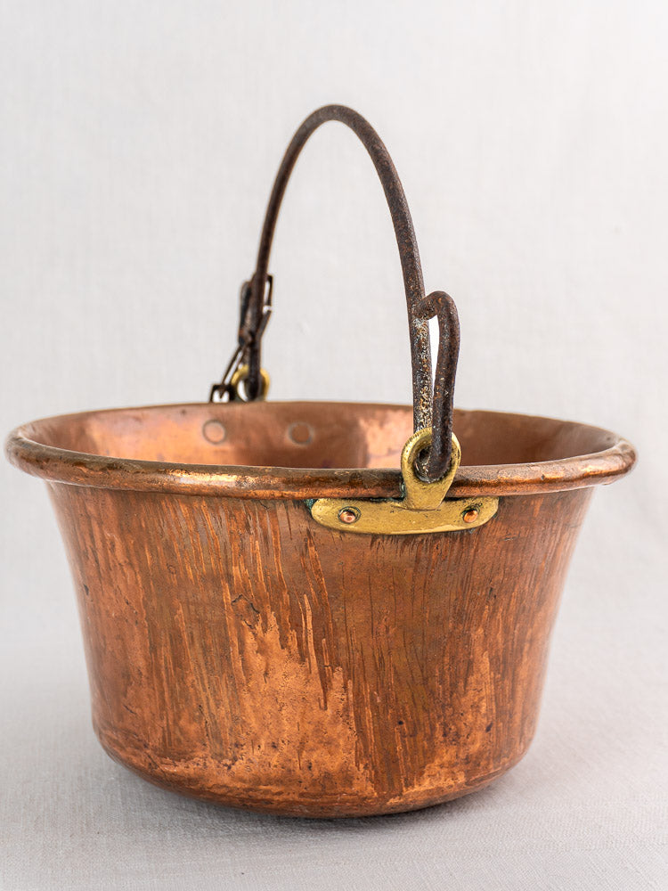 Antique French copper hearth pot with wide rim and iron bail handle on light background.
