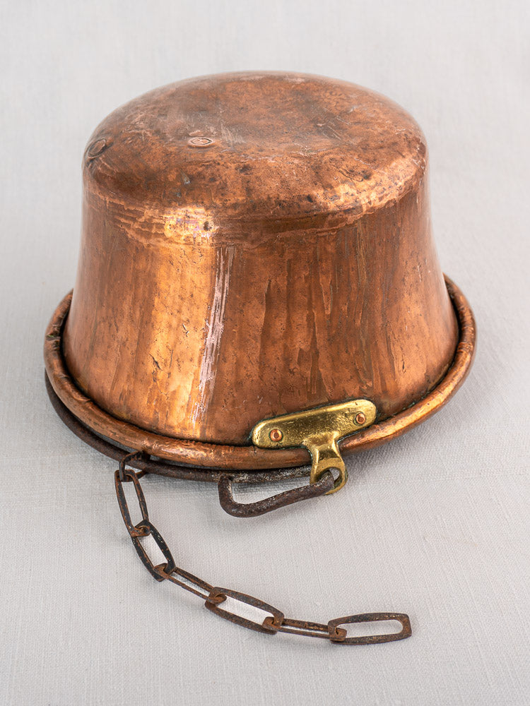 Antique French copper hearth pot upside down on white surface, displaying iron bail handle and chain.