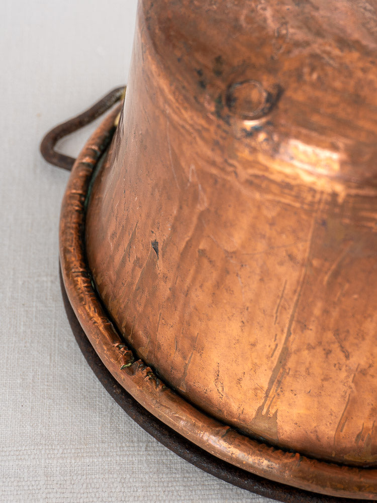 Antique French copper hearth pot with iron bail handle and chain on light textured surface.
