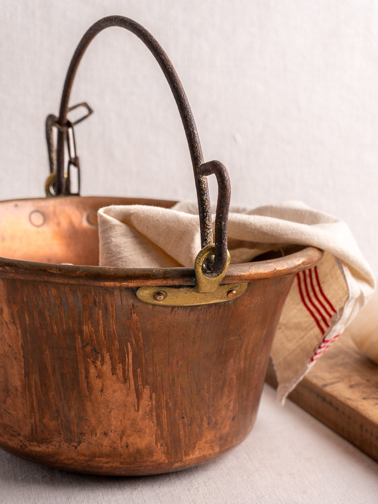 Antique French copper hearth pot with iron bail handle, draped with cream cloth and red stripes.