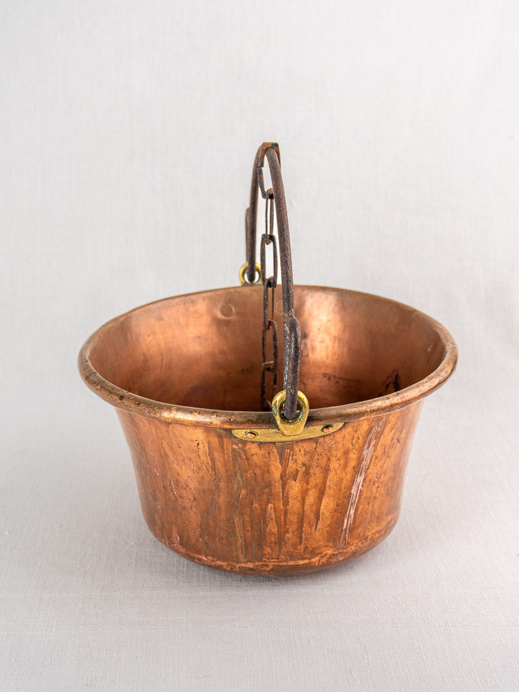 Antique French copper hearth pot with rounded base and iron bail handle, on light background.