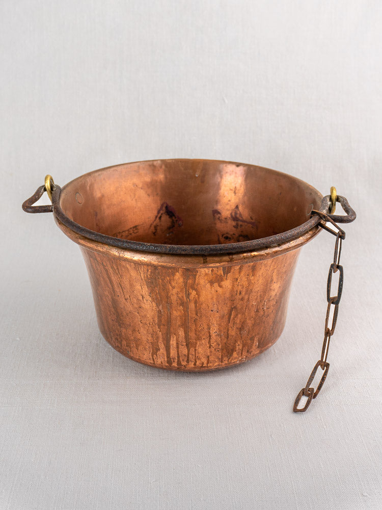 Antique French copper hearth pot with iron bail handle and chain on a light surface.
