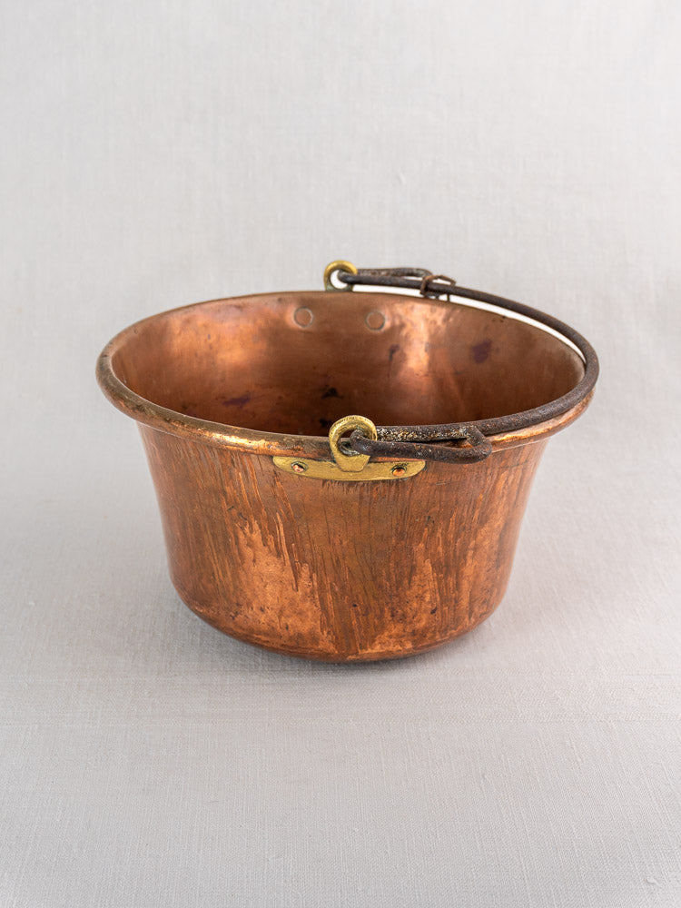 Antique French copper hearth pot with weathered surface and iron bail handle on neutral background.