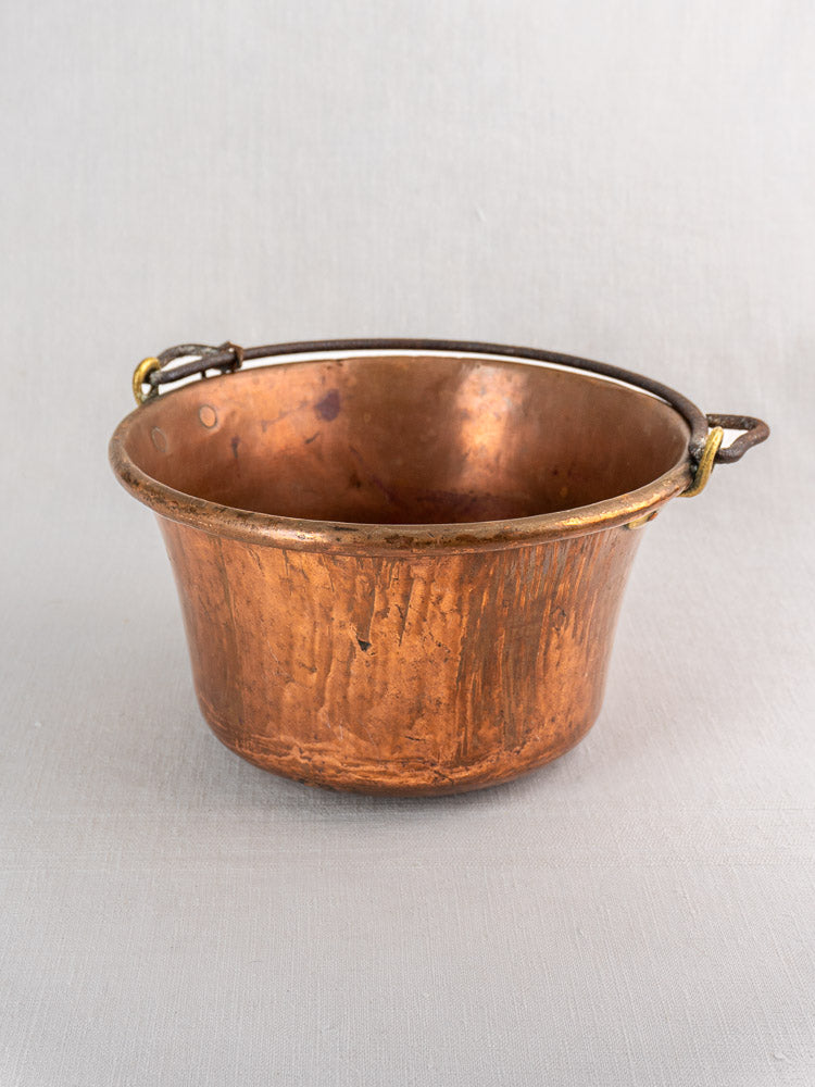 Antique French copper hearth pot with rounded base, iron bail handle, and chain on light gray surface.