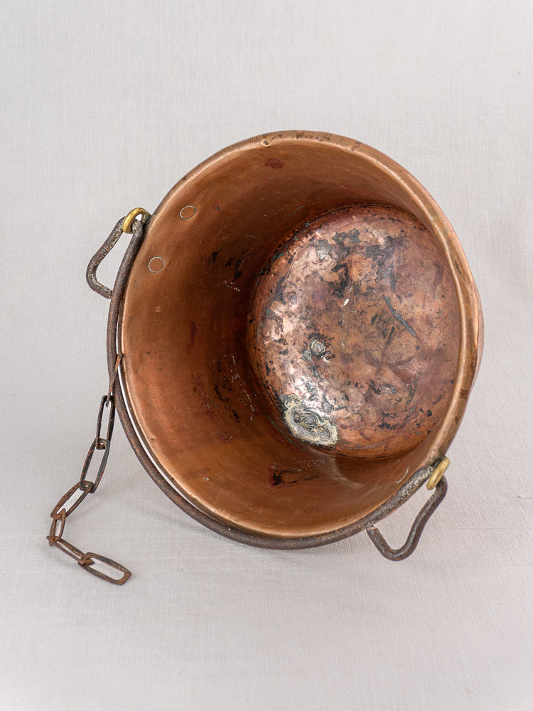 Antique French copper hearth pot with iron bail handle and chain, tarnished interior, on neutral background.