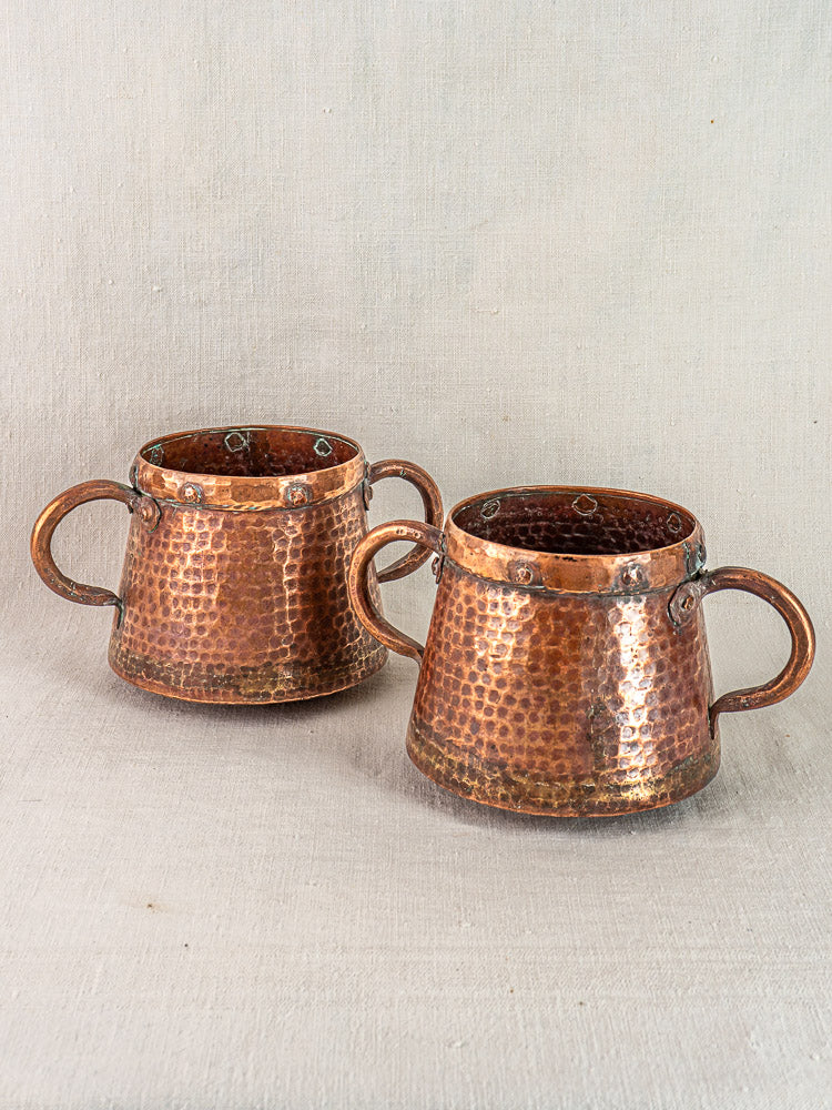 Pair of antique French hand-hammered copper pots from 1880–1920 displayed on textured linen surface.