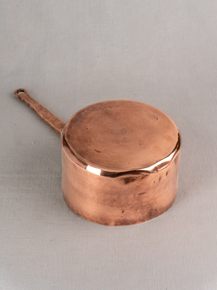 18th-century French copper preserving pot with flat base and hand-forged handle, shown upside down on light grey surface.