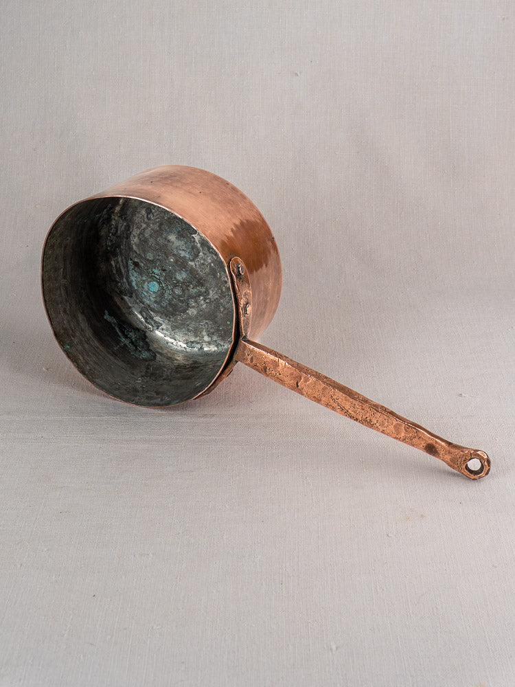 18th-century French copper preserving pot with solid handle and hand-forged rivets on light gray fabric.