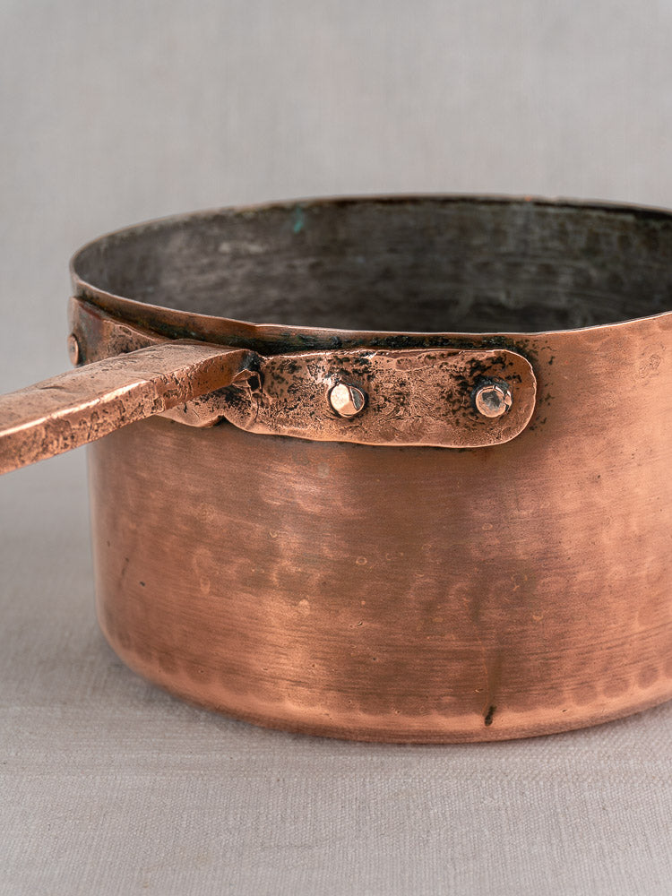 Antique French copper preserving pot with rustic patina, tarnish, and a solid handle fastened by hand-forged rivets.