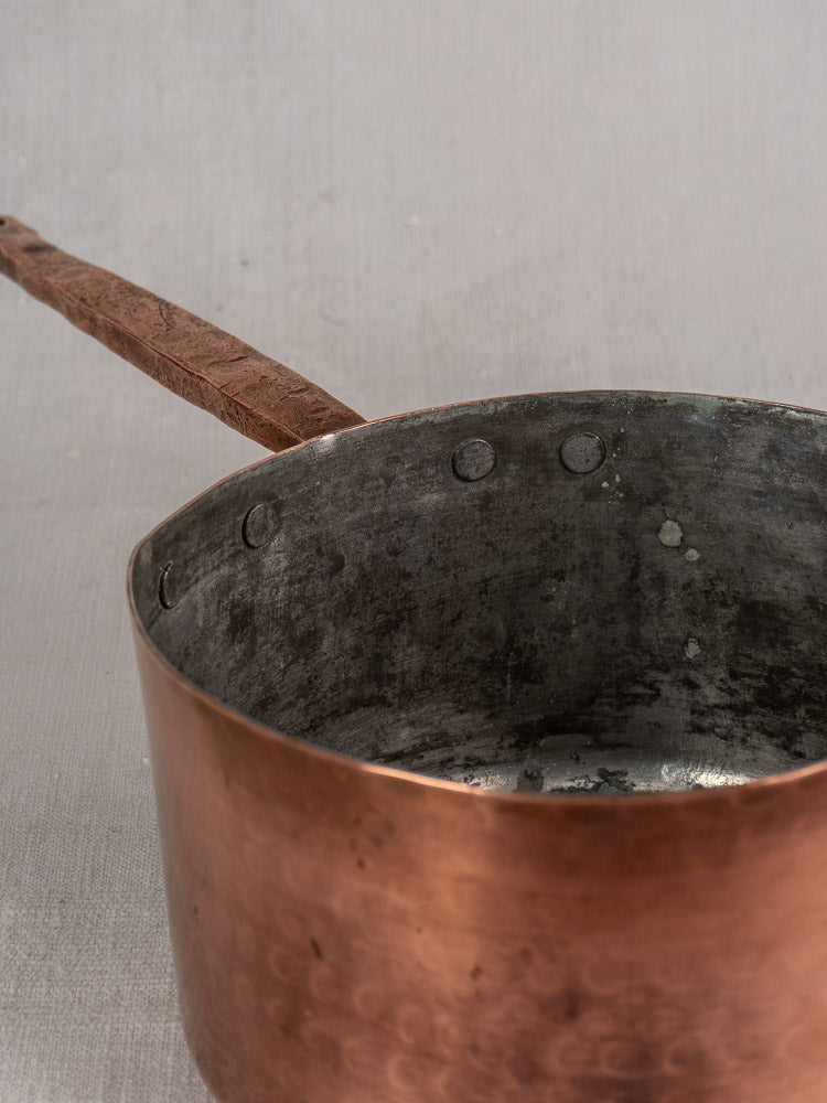 Antique French copper preserving pot with solid handle, hand-forged rivets, and weathered interior on neutral background.