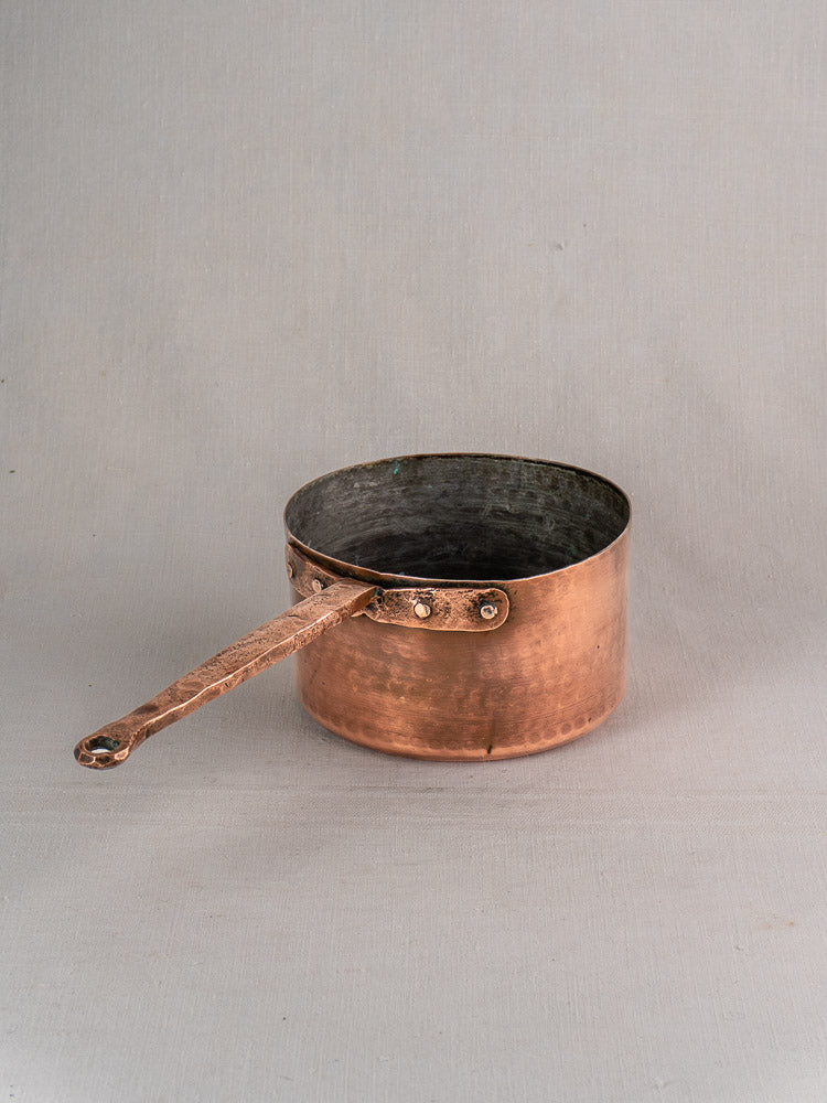 18th century French copper preserving pot with solid handle, hand-forged rivets, slightly tarnished interior on gray background.