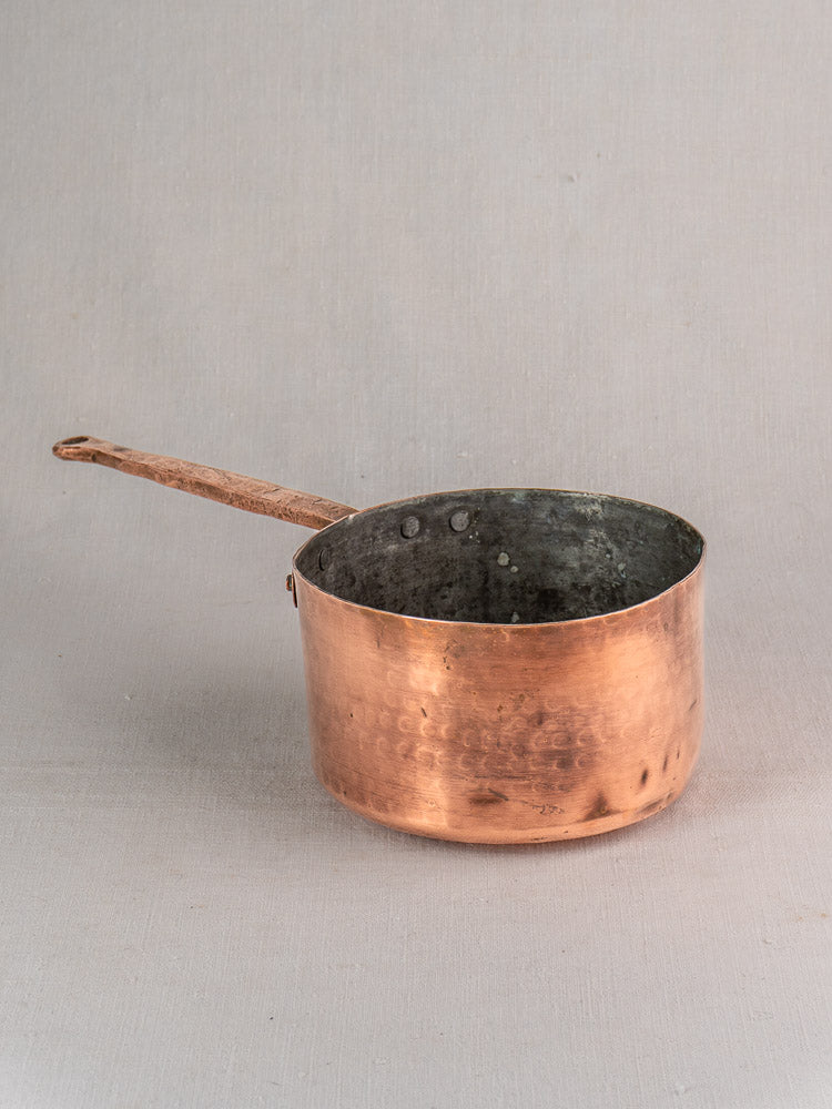 18th-century antique French copper preserving pot with solid handle and hand-forged rivets on a light gray surface.