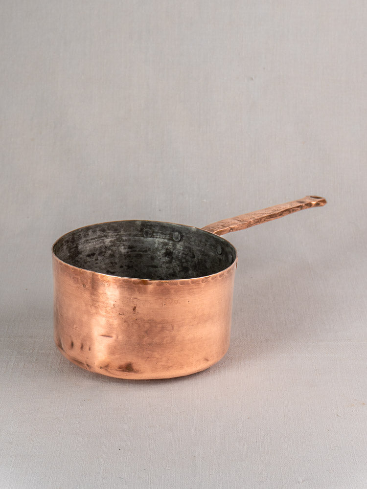 Antique French copper preserving pot with hand-forged rivets and a long handle on a light gray background.