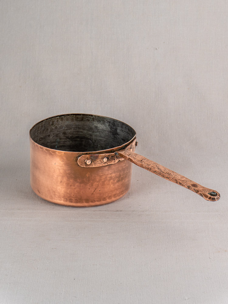 Antique French copper preserving pot with solid copper handle on a neutral gray surface and background.