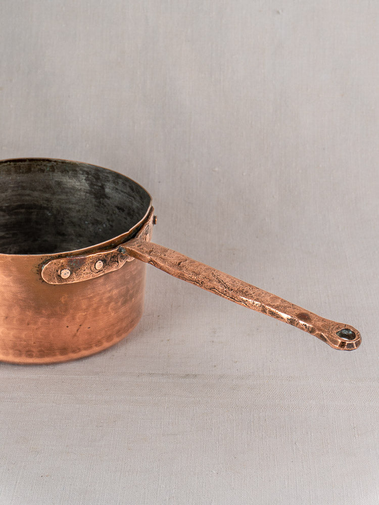 Antique French copper preserving pot with solid copper handle, partially visible on a light gray surface.