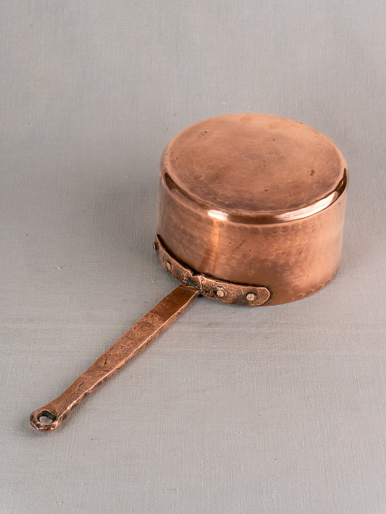 Antique French copper preserving pot with hand-forged rivets, rustic patina, on neutral gray surface.