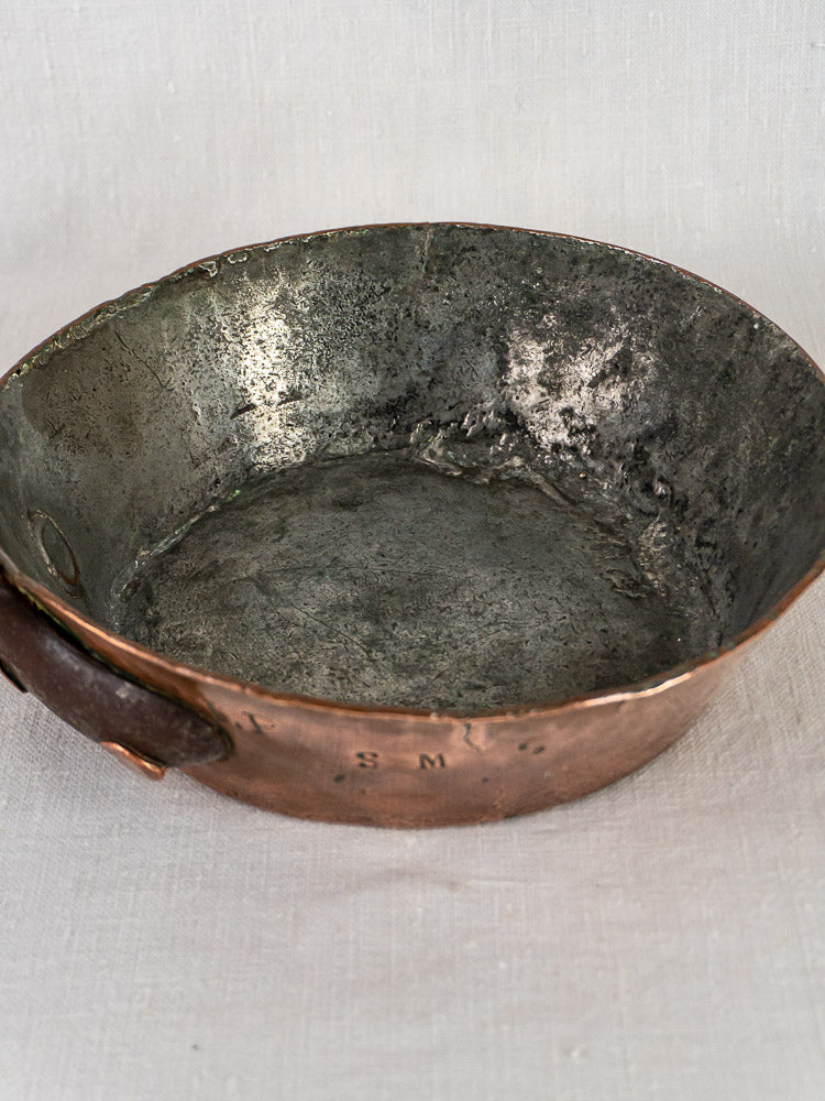Antique 19th-century French copper sauté pan with hand-hammering, tarnished silver interior, and side handle on fabric.