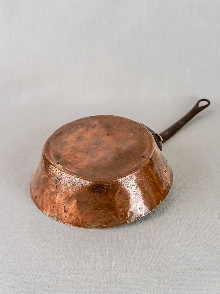Antique 19th-century French copper sauté pan with dark handle, rich patina, and subtle dents.