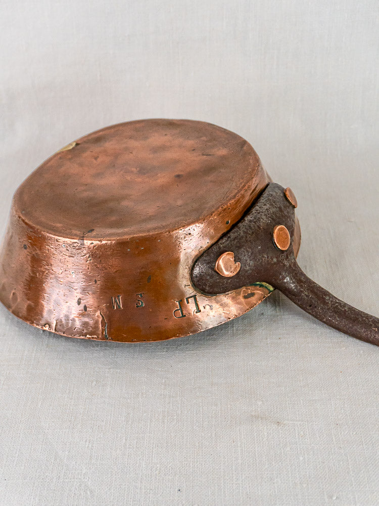 Antique 19th-century French copper sauté pan upside down, hand-hammered base and engraved S.M. initials visible.