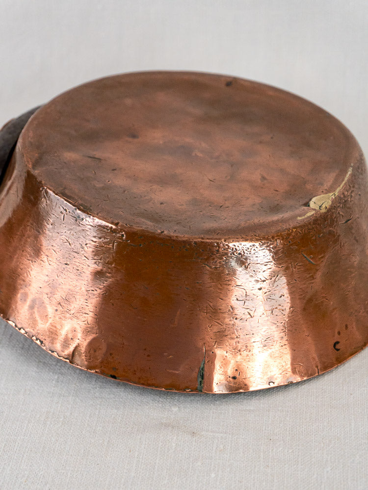 Antique 19th-century French copper sauté pan upside down, showing age-related scratches and dents on light fabric.