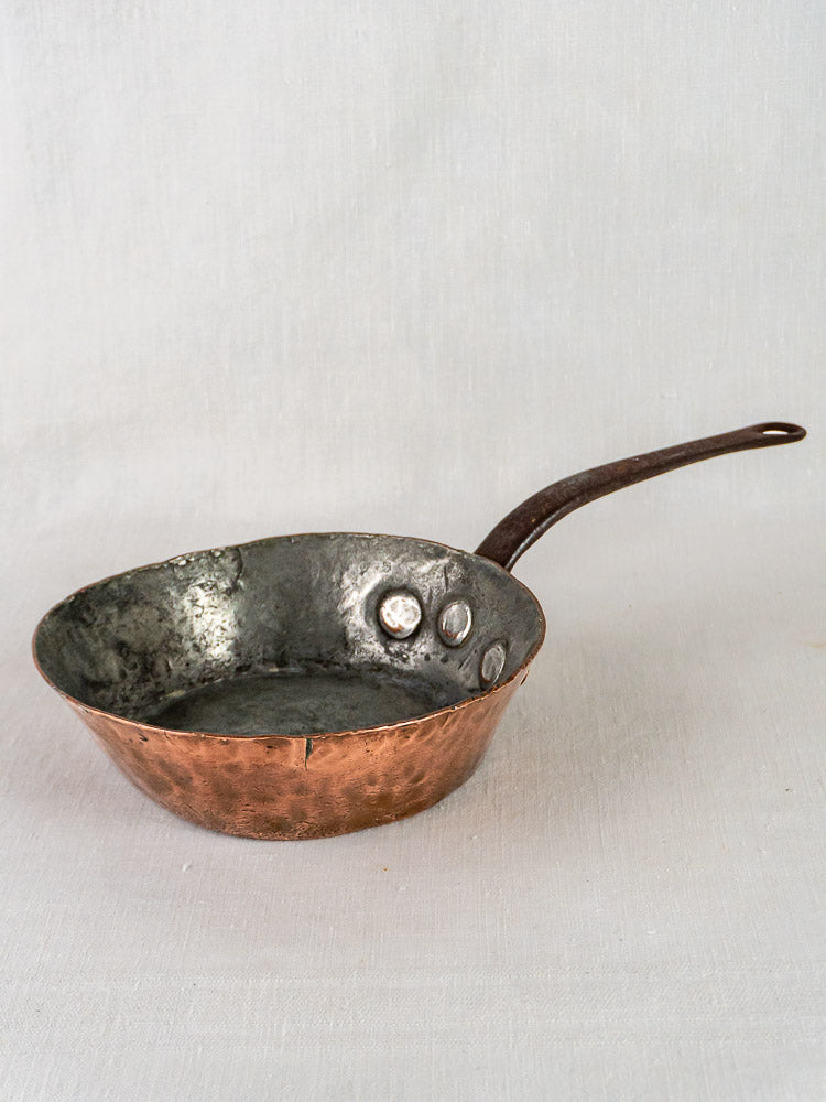 Antique French 19th-century copper sauté pan with hand-hammered finish and dark metal handle on light background.