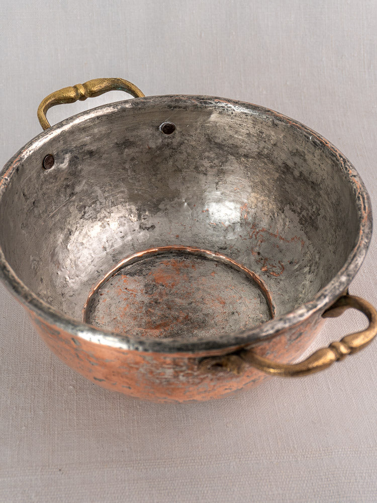 Antique French copper bowl with ornate brass handles and a weathered, scratched interior for rustic charm.