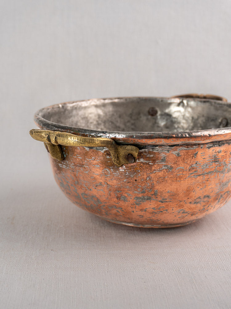 Antique French copper bowl with brass handles, silver-toned interior, and aged patina on a neutral textured surface.