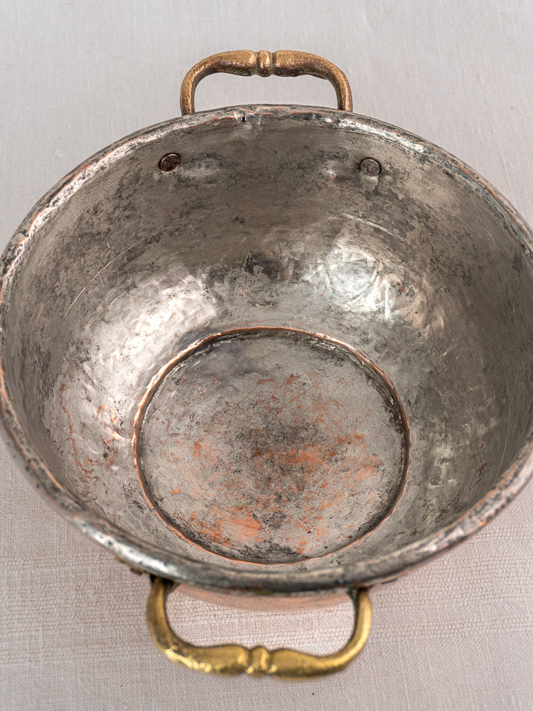 Antique French copper bowl with ornate brass handles, early 19th century, aged patina, on light textured surface.
