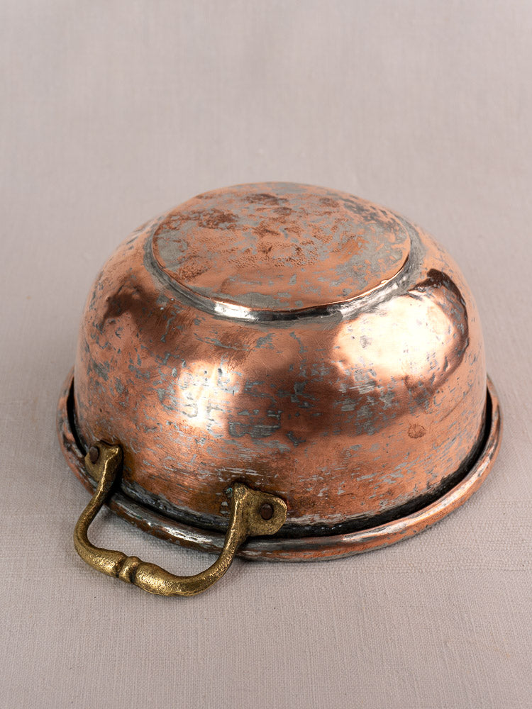 Antique French copper bowl with brass handles, early 19th century, upside-down, tarnished with worn silver patches on neutral fabric.