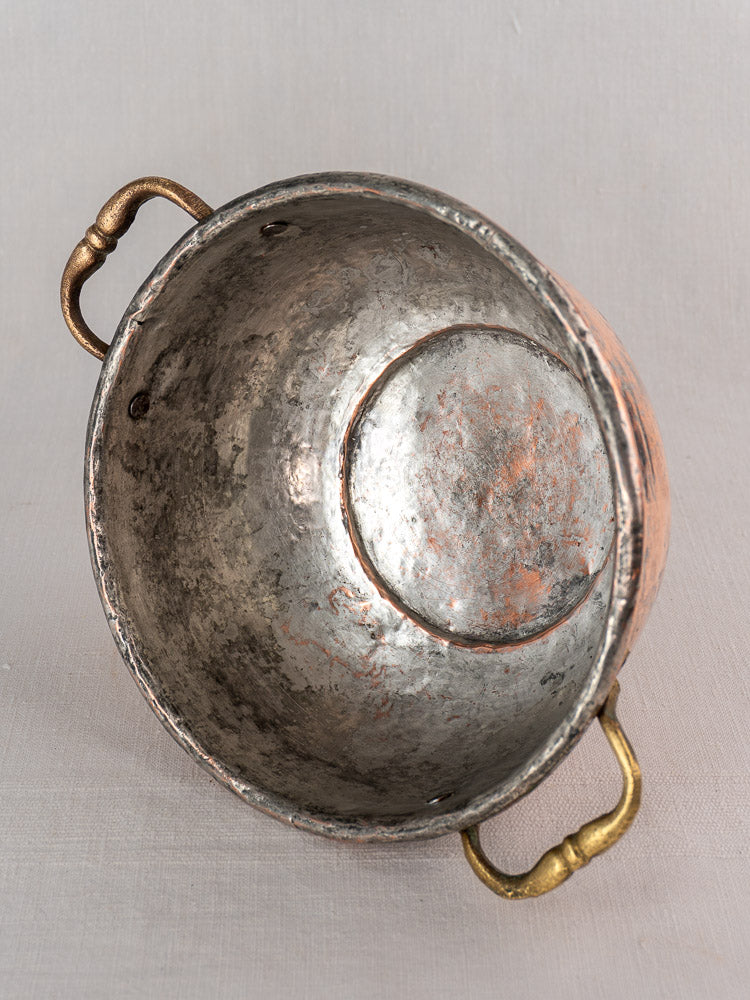 Early 19th-century French copper bowl with brass handles, weathered exterior, and silver-copper interior, shown tilted on its side.