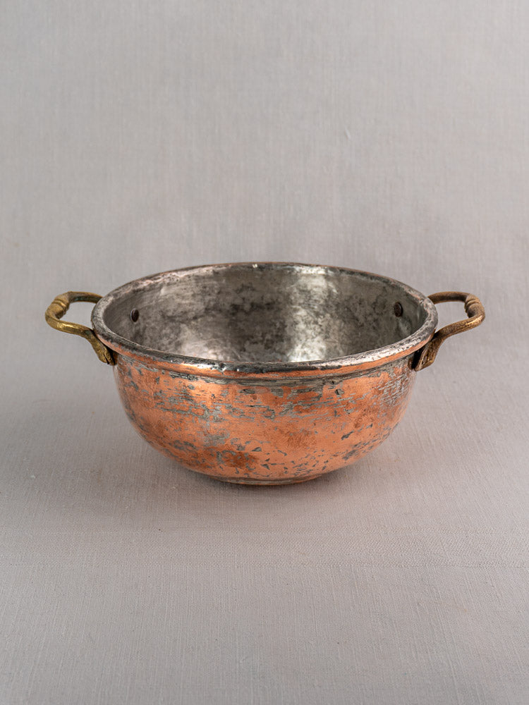 Early 19th-century French copper bowl with brass handles, tarnished, on neutral fabric and light grey background.