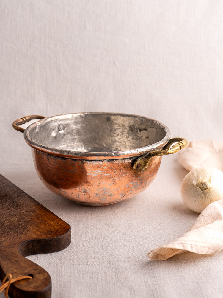 Antique French copper bowl with brass handles, early 19th century, patina and wear; on light fabric with wood board and onion.