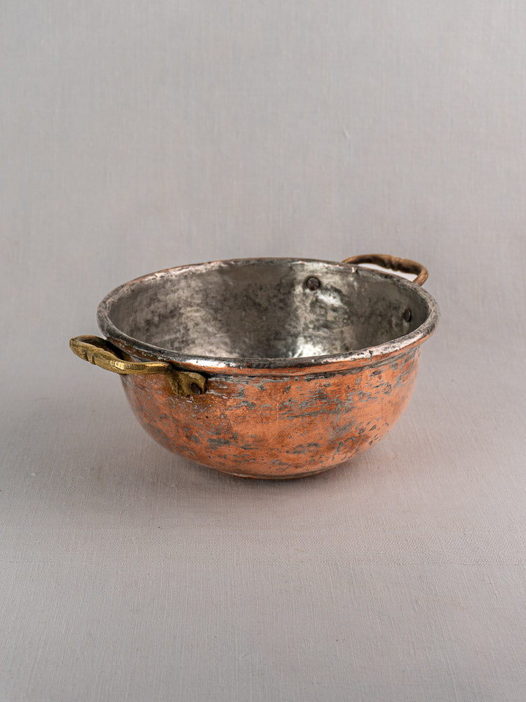 Antique French copper bowl with brass handles and silver-toned interior on a gray surface, plain background.