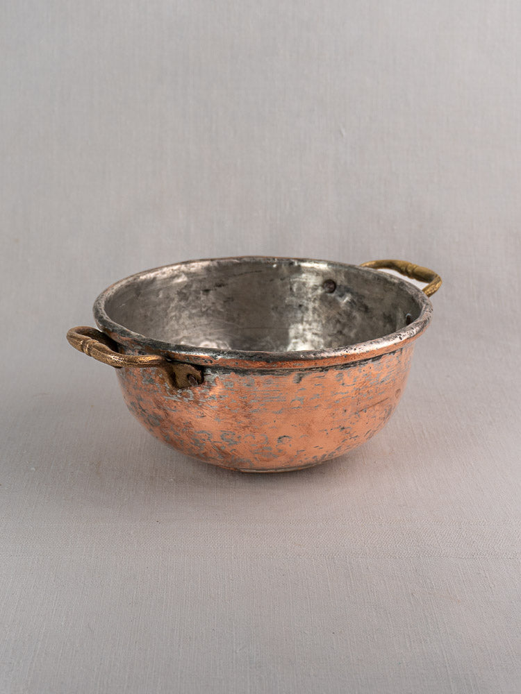 Antique French copper bowl with brass handles, silver-toned interior, hand-formed patina, on neutral fabric.