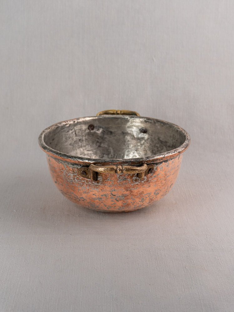 Antique French copper bowl with brass handles and tarnished silver interior on a light gray background.