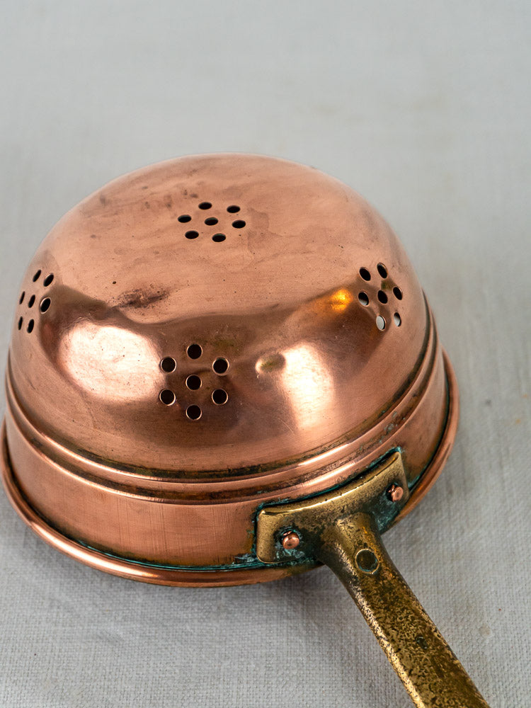Antique French graduated copper strainers with brass handles, displayed upside down on a light gray surface.