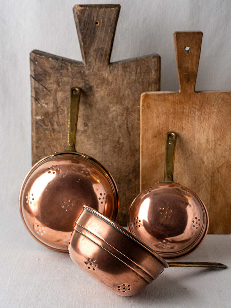 Antique French copper strainers, graduated set of three with brass handles, on white background.
