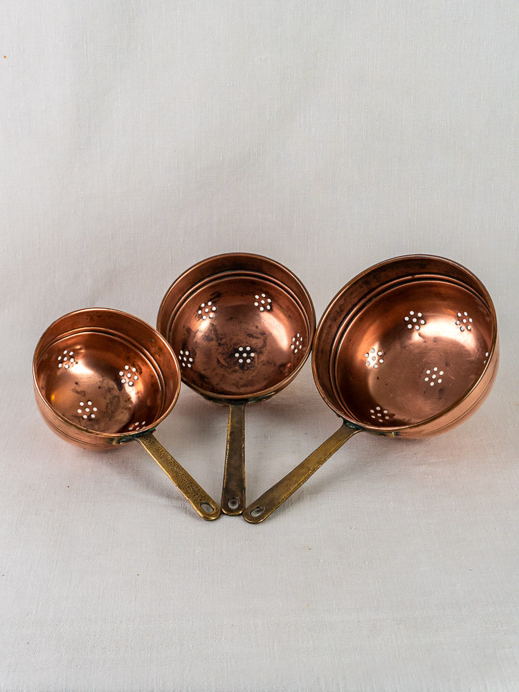 Antique French copper strainers, graduated set of three with brass handles, on white background.