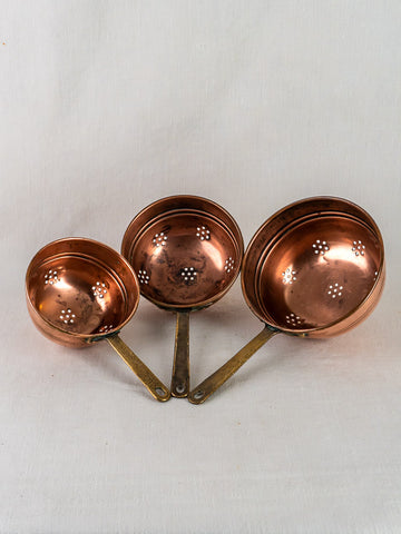 Antique French copper strainers, graduated set of three with brass handles, on white background.