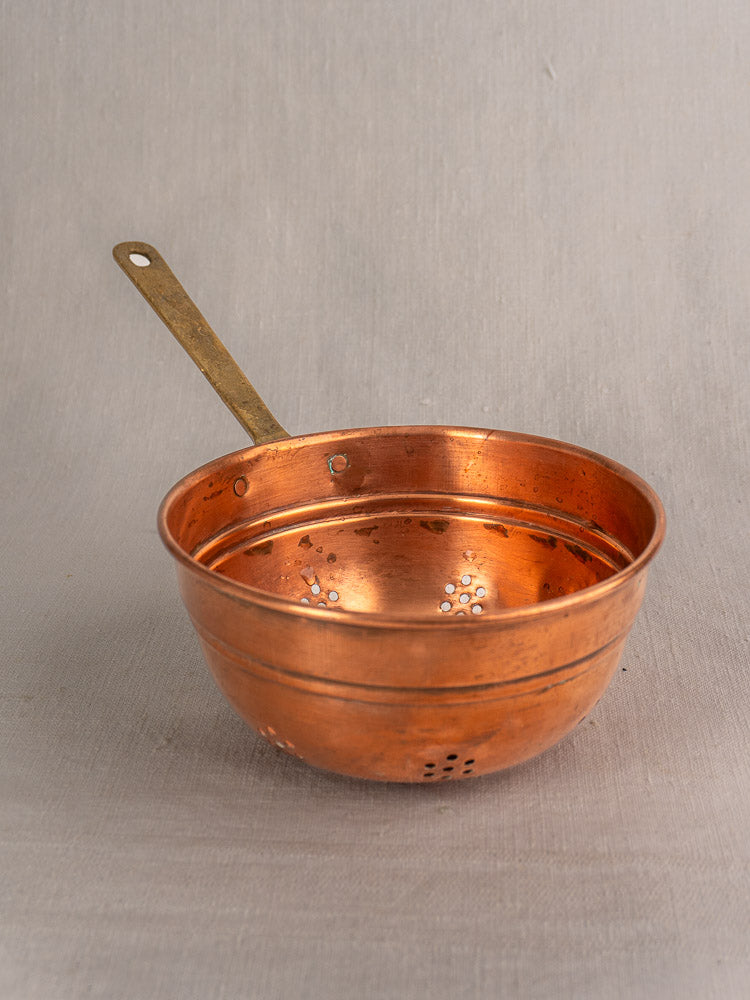 Set of three antique French copper colanders with brass handles, gently tarnished, on a neutral gray surface.