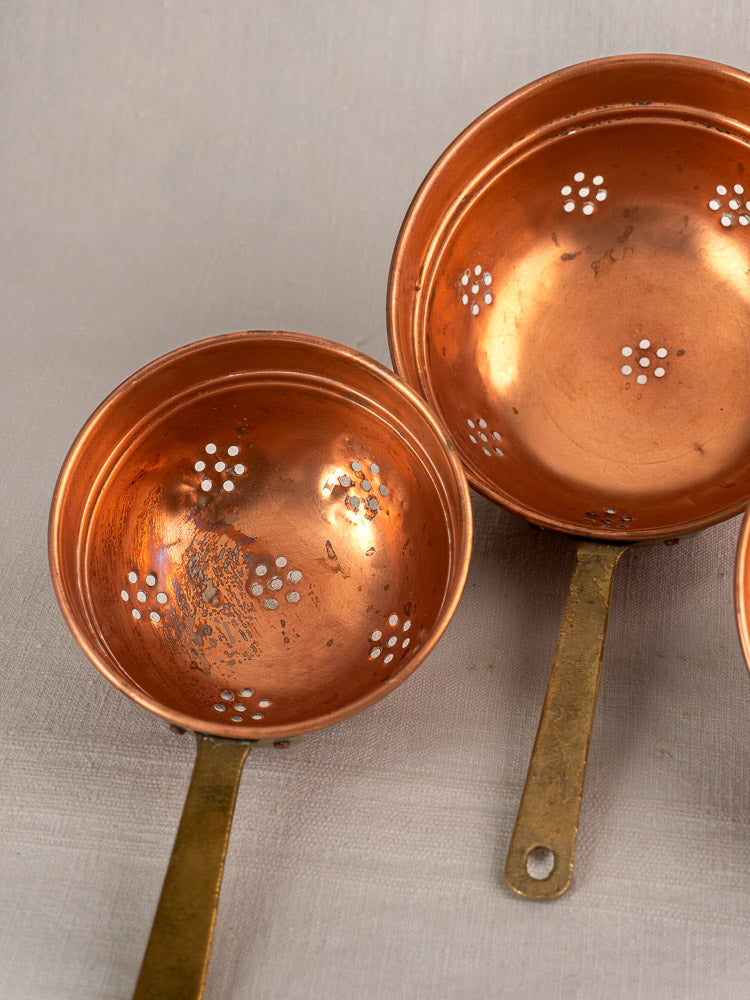 Antique French copper strainer set of three colanders with brass handles and circular pierced patterns.