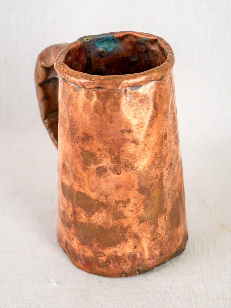 Antique French hand-forged copper tankard with hammered finish and wide handle on a neutral background.