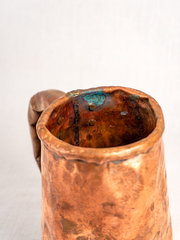 Hand-forged antique French copper tankard with hammered texture, curved handle, and visible patina.